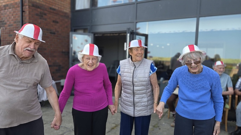a group of residents with England hats on holding hands and smiling outside